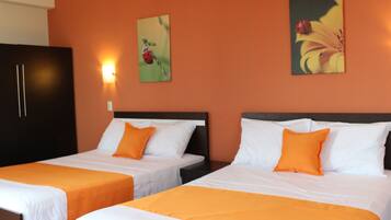 Two twin beds with orange bedding, a dark wardrobe, and two wall-mounted paintings.