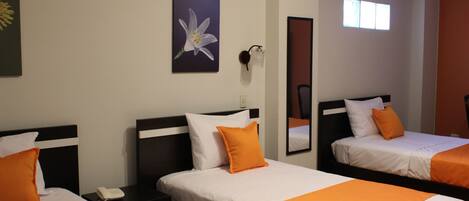 A hotel room with two beds, each with white bedding and orange accents, a nightstand with a phone, a wall-mounted lamp, a framed flower painting, and a window with natural light.
