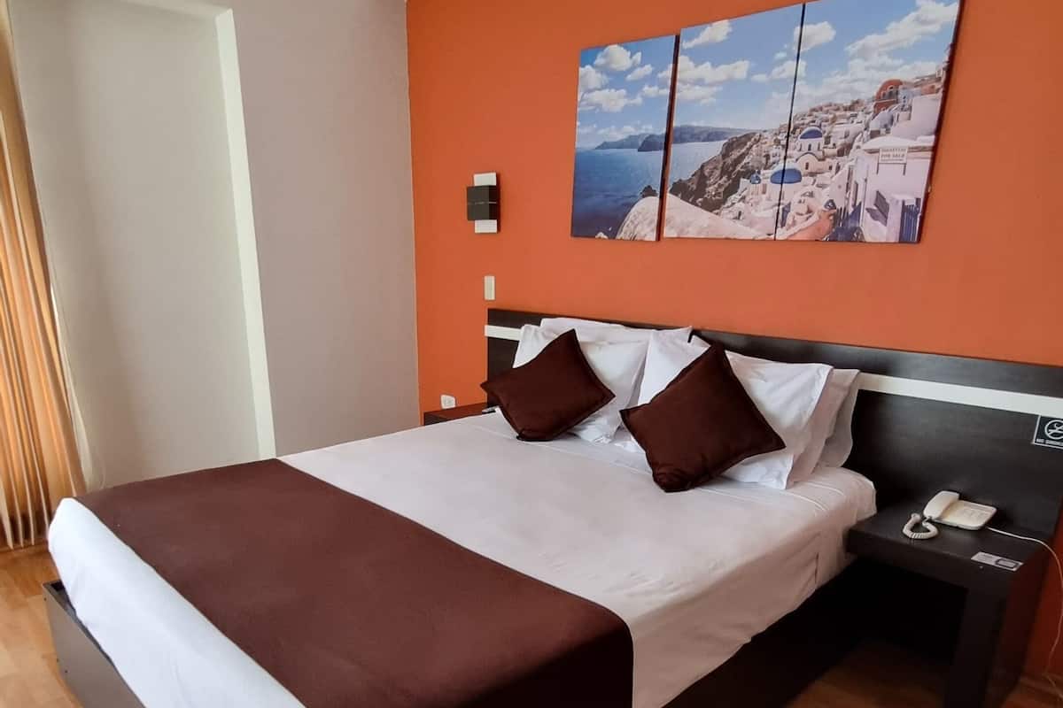 Una habitación de hotel moderna con una cama grande, suelo de madera, una mesita de noche con un teléfono y un cuadro en la pared.