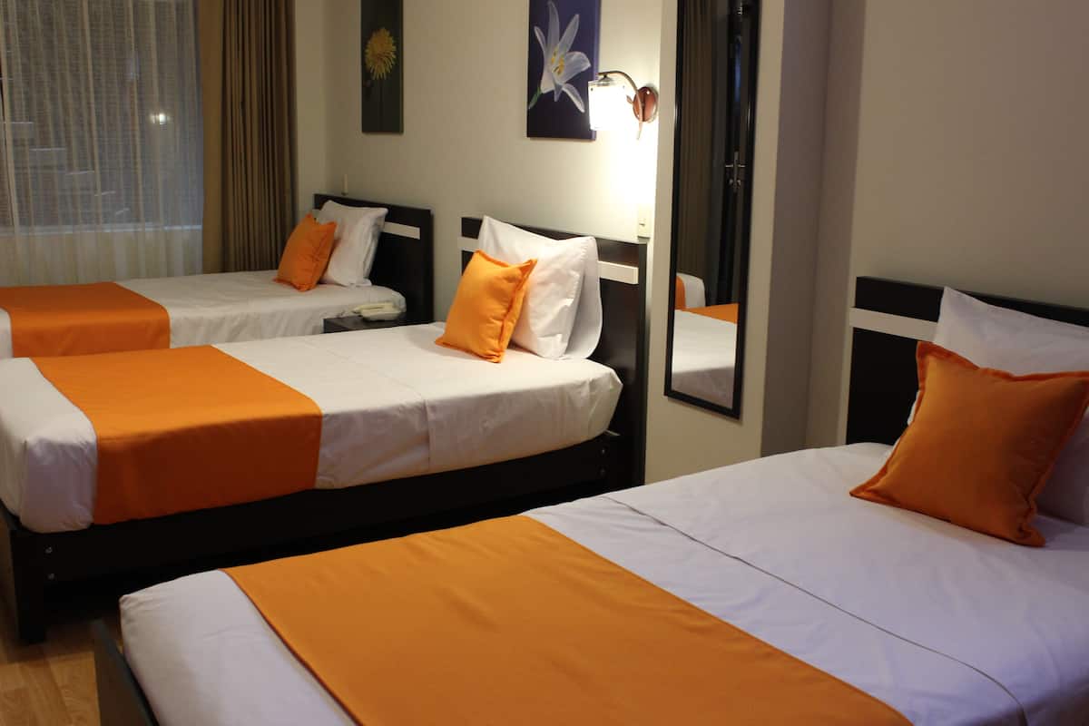 Habitación de hotel con tres camas, cada una con ropa blanca y detalles color naranja.
