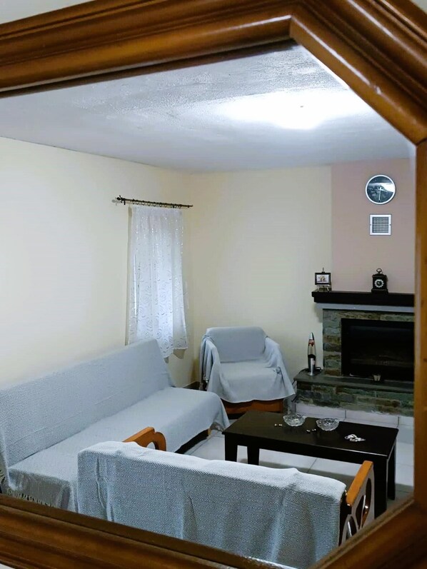 Een woonkamer met een bank, twee fauteuils, een salontafel, een open haard en een klok aan de muur.