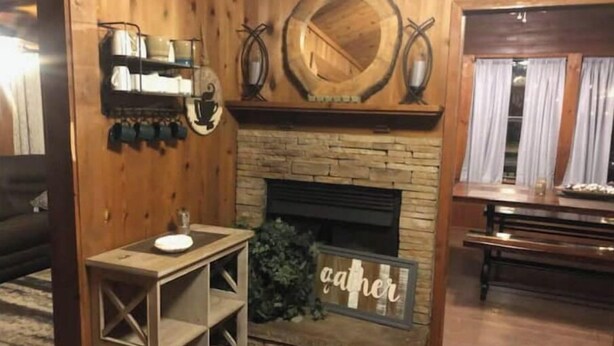 A cozy living room with a stone fireplace, wooden walls, and a 'Gather' sign.