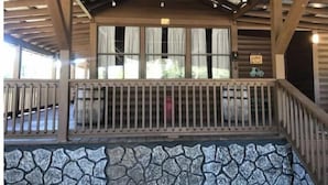 A covered outdoor area with a stone wall, wooden railing, and a window with curtains.