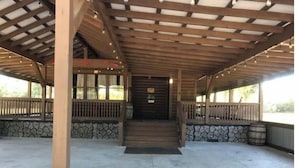 A covered outdoor area with a stone wall, wooden railing, and a central staircase leading to a door.