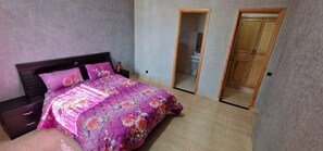 A bedroom with a bed, nightstands, a wooden wardrobe, and a door leading to a bathroom. - aqua villa (Marrakesh)