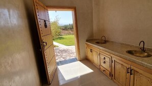 Cuina amb armaris de fusta, dos rentapesos i vista a un jardí a través d'una porta oberta.