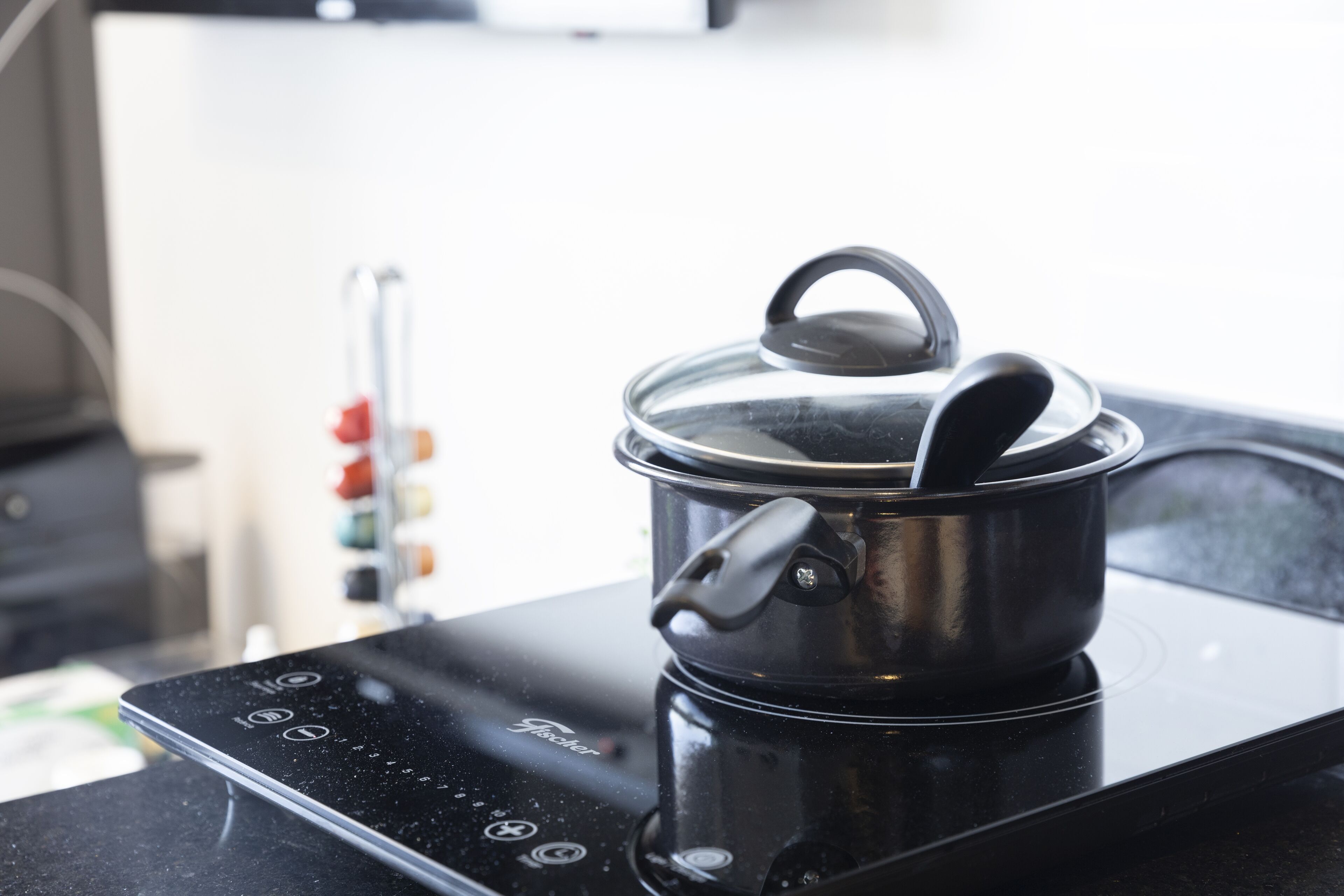 Una cocina con una placa de inducción negra, una olla con tapa y un panel de control de la estufa.