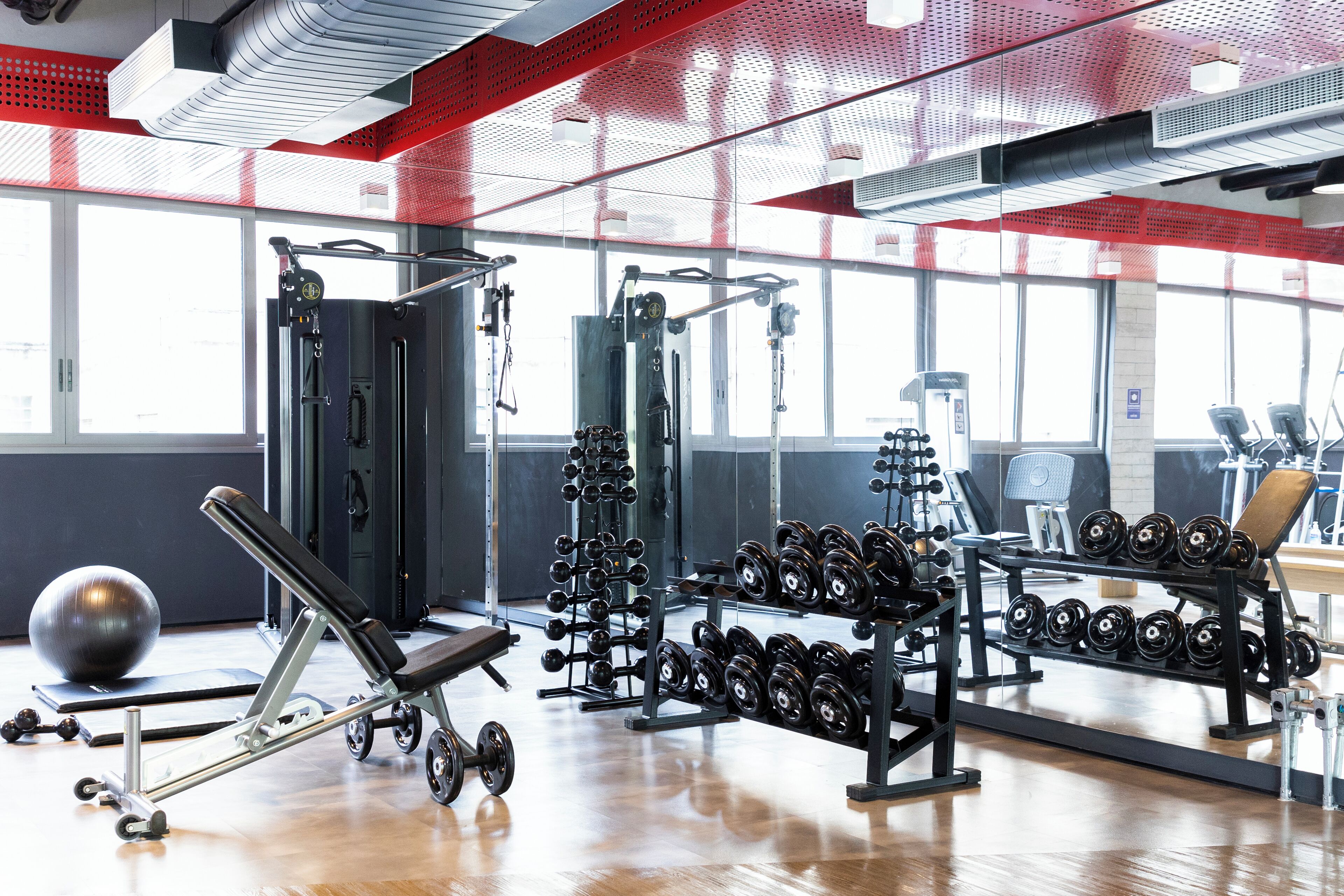 Een sportschool met diverse fitnessapparaten, waaronder gewichten, een bank en krachtapparaten.
