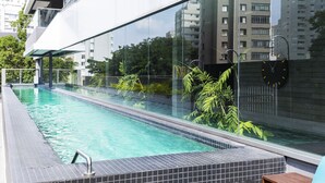 A modern swimming pool with clear water, surrounded by glass walls and plants, reflecting nearby buildings. - Oscar Freire - Condomínio Glass VN (São Paulo)