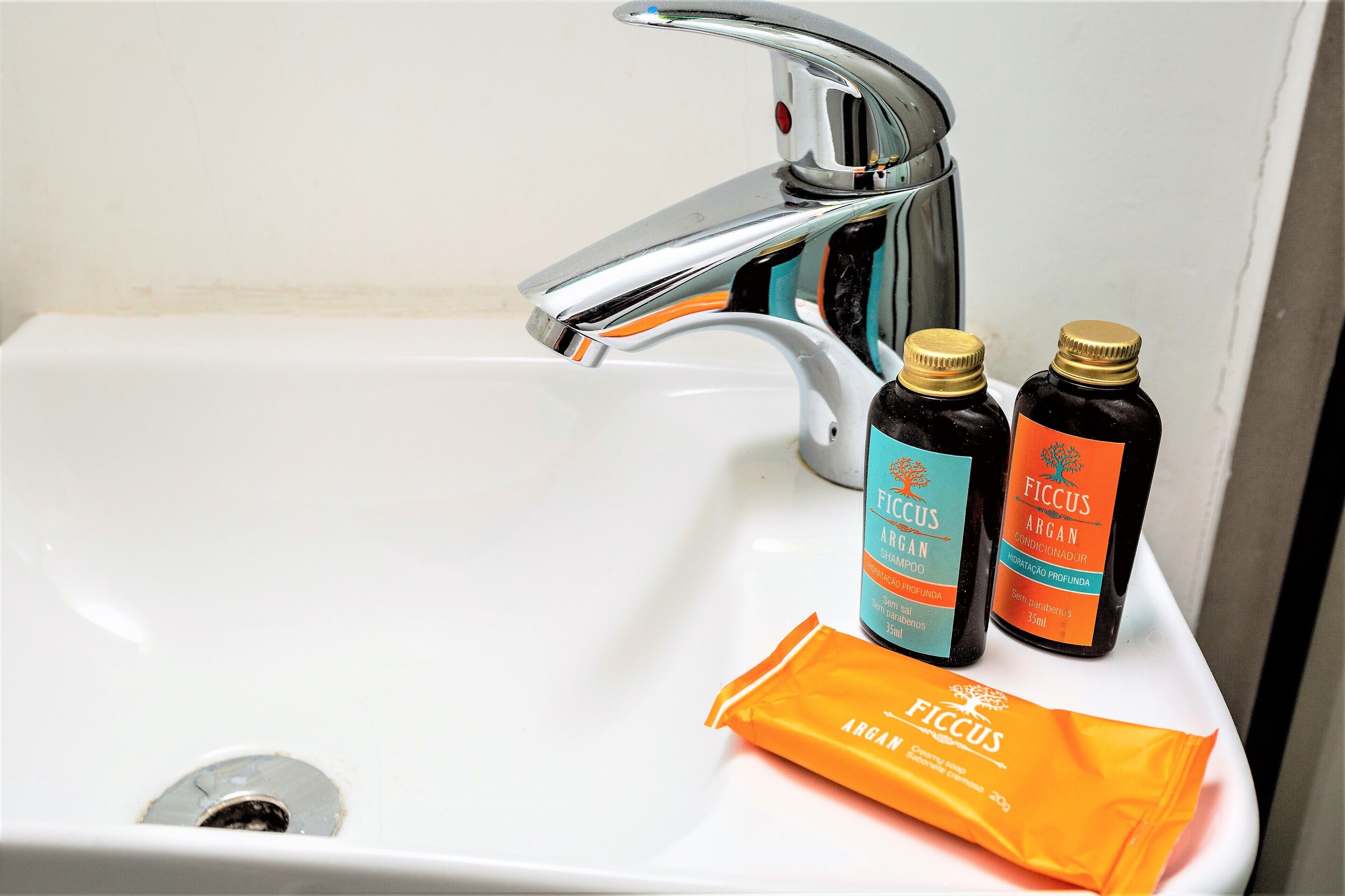 A bathroom sink with two bottles of Ficus Argan shampoo and an orange bottle of shampoo.
