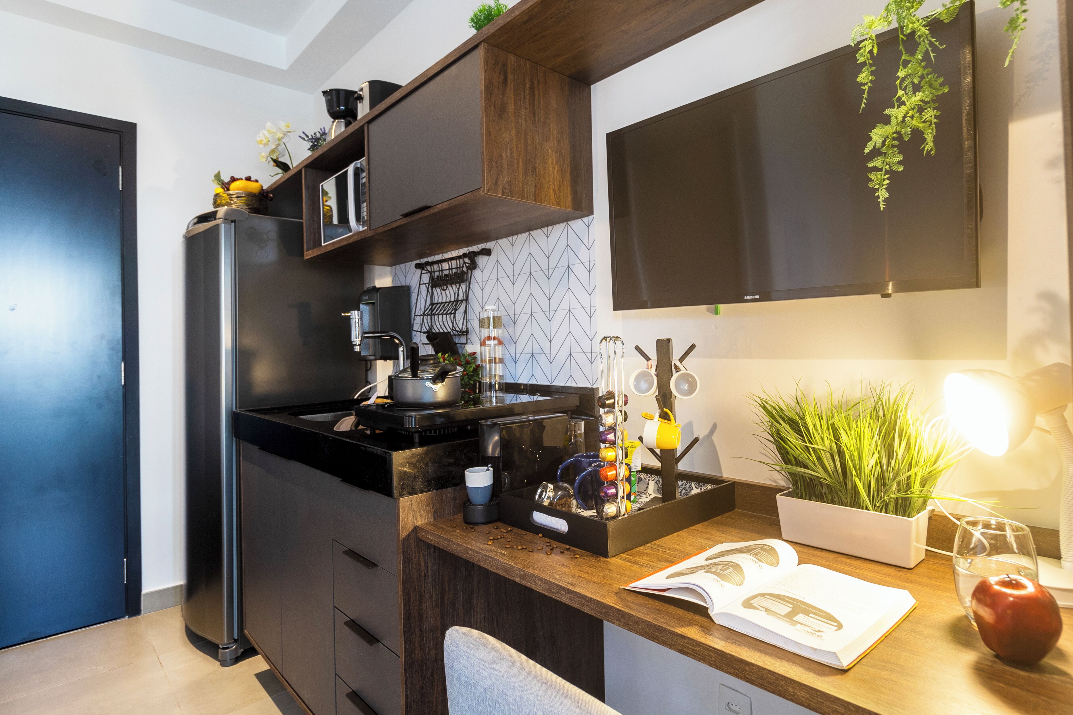 A modern kitchen with a built-in refrigerator, a coffee machine, and a countertop with a book, a glass, and a potted plant.