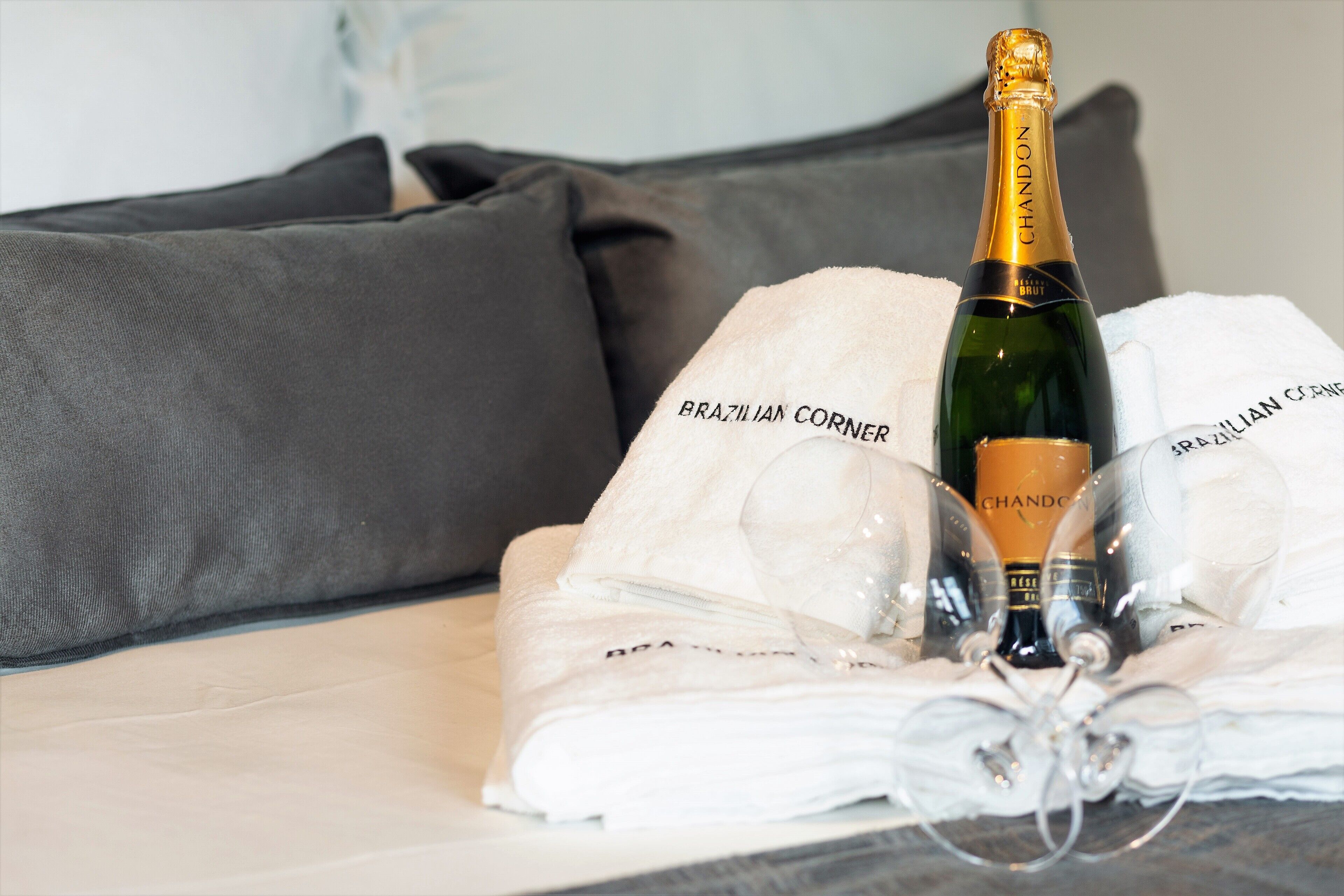 A bottle of Chandon champagne, two glasses, and a towel with "Brazilian Corner" text on a bed.
