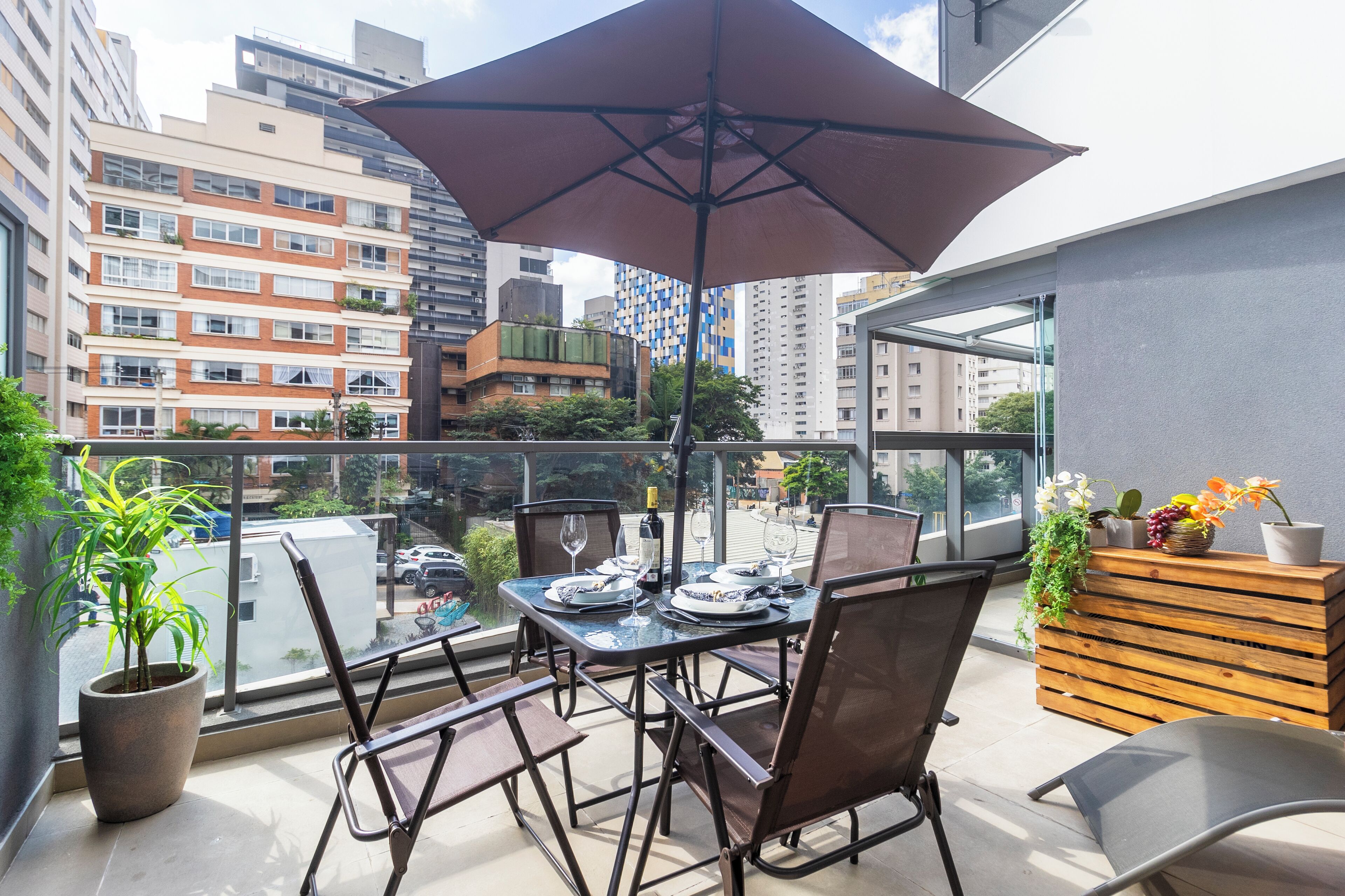 A balcony with a table set for dining, potted plants, and a view of the cityscape.