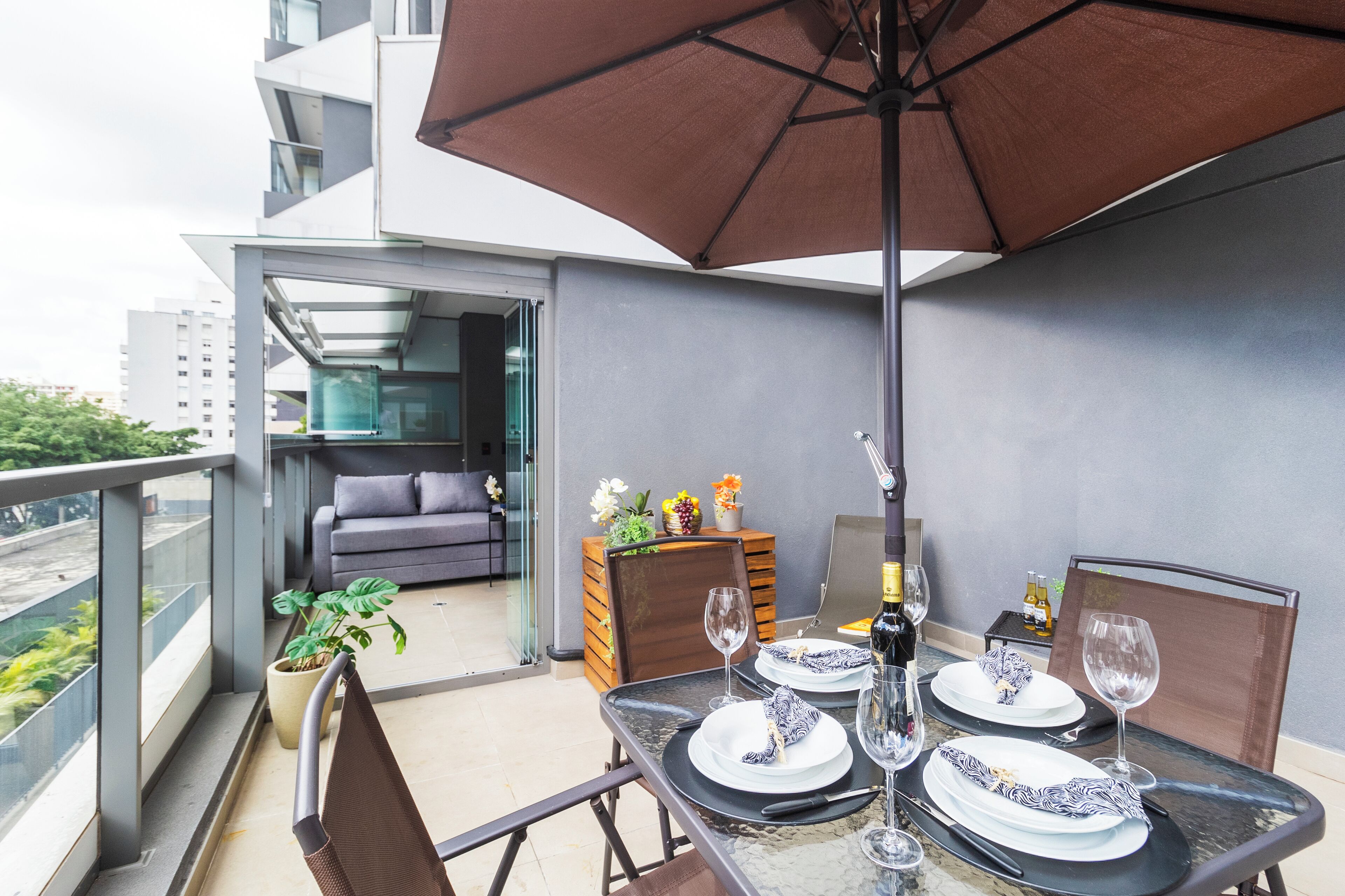 A balcony with a dining table set for two, a sofa, and a potted plant.