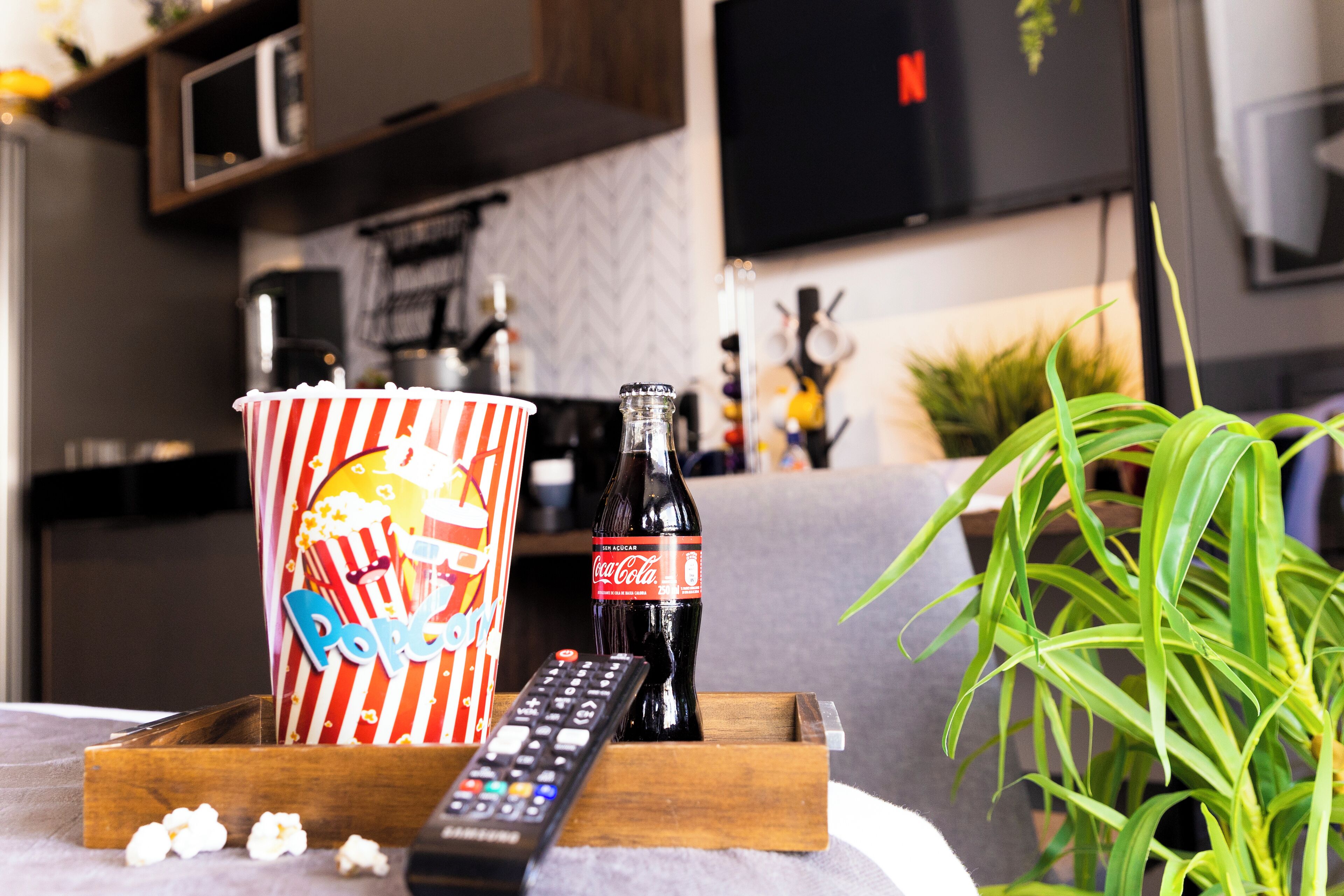 Una bandeja de madera con un cubo de palomitas, una botella de Coca-Cola y un control remoto.