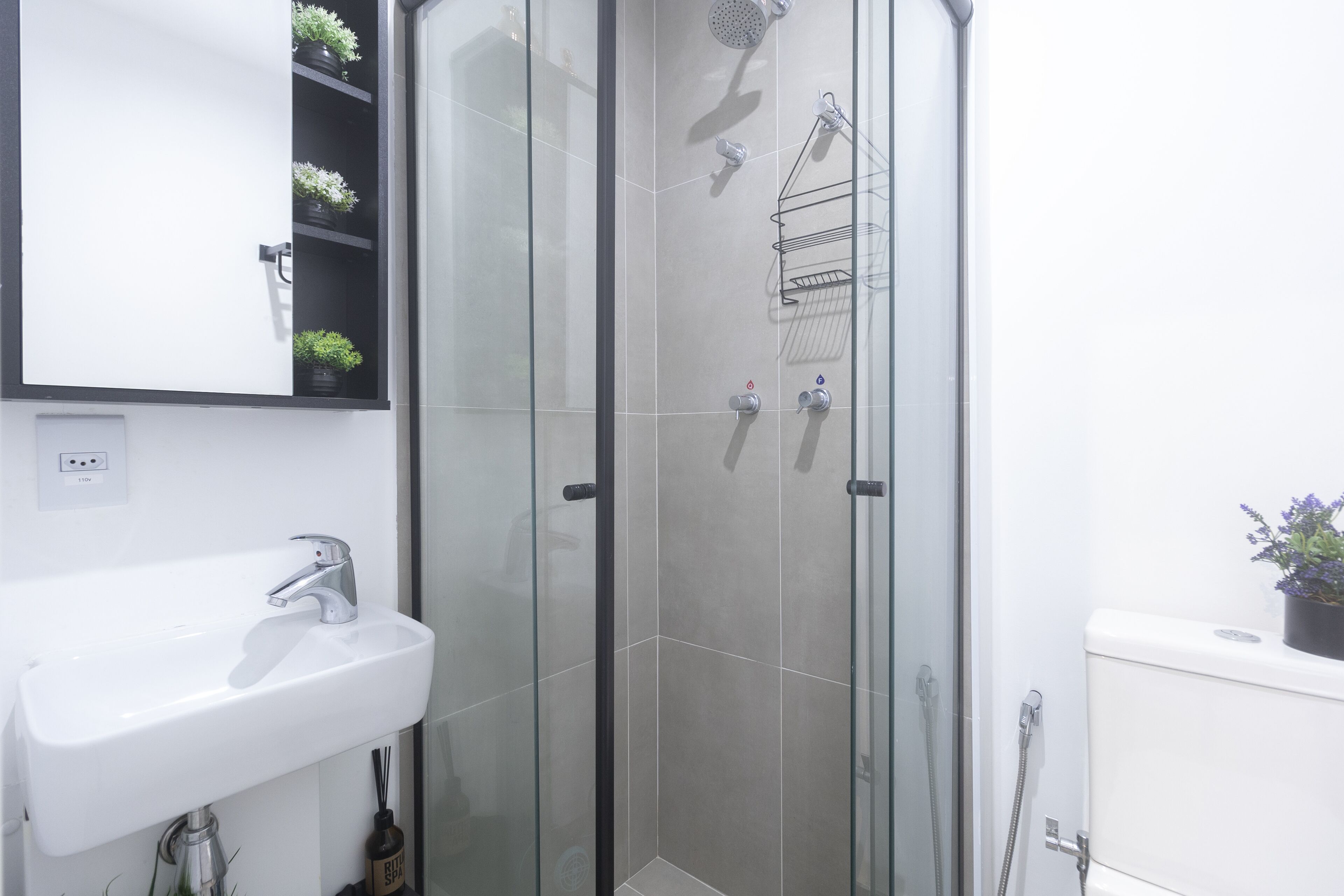 A bathroom with a glass-enclosed shower, a white sink, and a mirror above the sink.