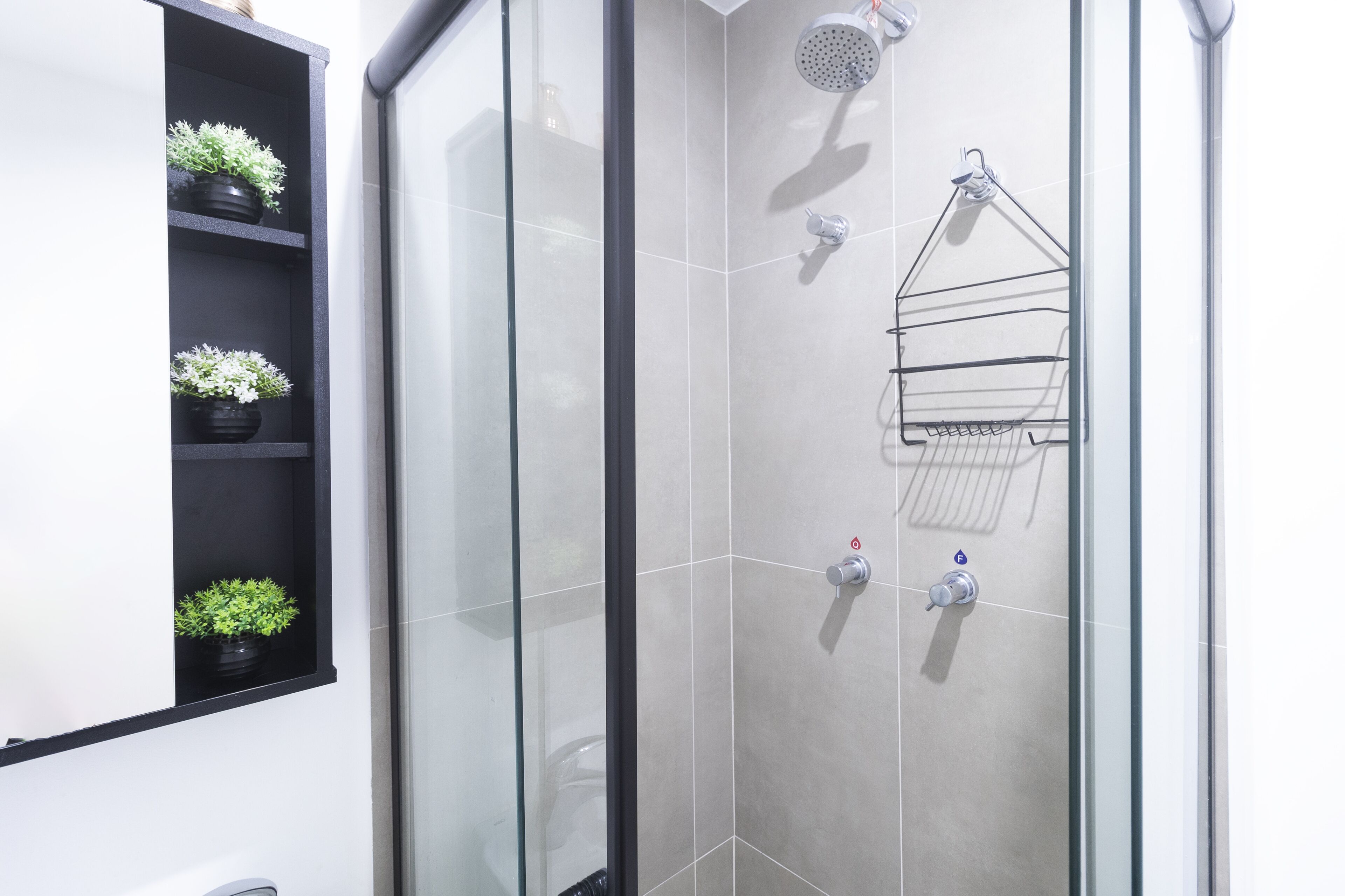 Un baño moderno con cabina de ducha de vidrio, un estante negro con plantas en macetas y un perchero para toallas.