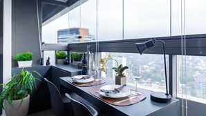A modern dining area with a table set for two, featuring a city view through large windows. - Oscar Freire - Condomínio Glass VN (São Paulo)