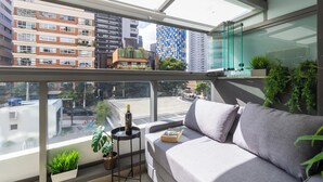 A modern balcony with a grey sofa, a small table with a wine bottle, and potted plants. - Oscar Freire - Condomínio Glass VN (São Paulo)