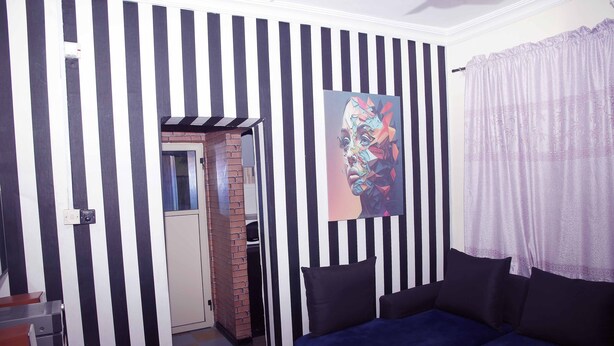 A room with a striped wall, a blue sofa, a painting, and a door leading to another room. - Smilley's Place Cosy accommodation close to Unilag (Lagos)