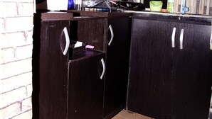 A kitchen with dark wooden cabinets, a tiled backsplash, and a patterned curtain. - Smilley's Place Cosy accommodation close to Unilag (Lagos)