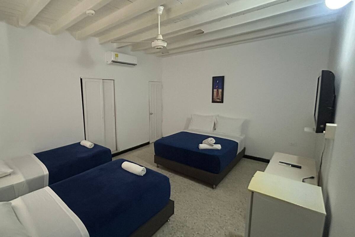 A hotel room with two single beds, a desk, a chair, an air conditioning unit, and a ceiling fan.