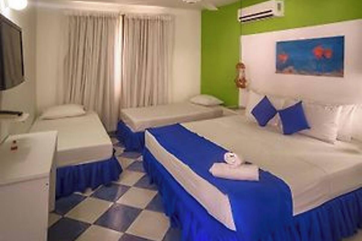 A hotel room with two beds, a checkered floor, a green accent wall, and a painting above the beds.
