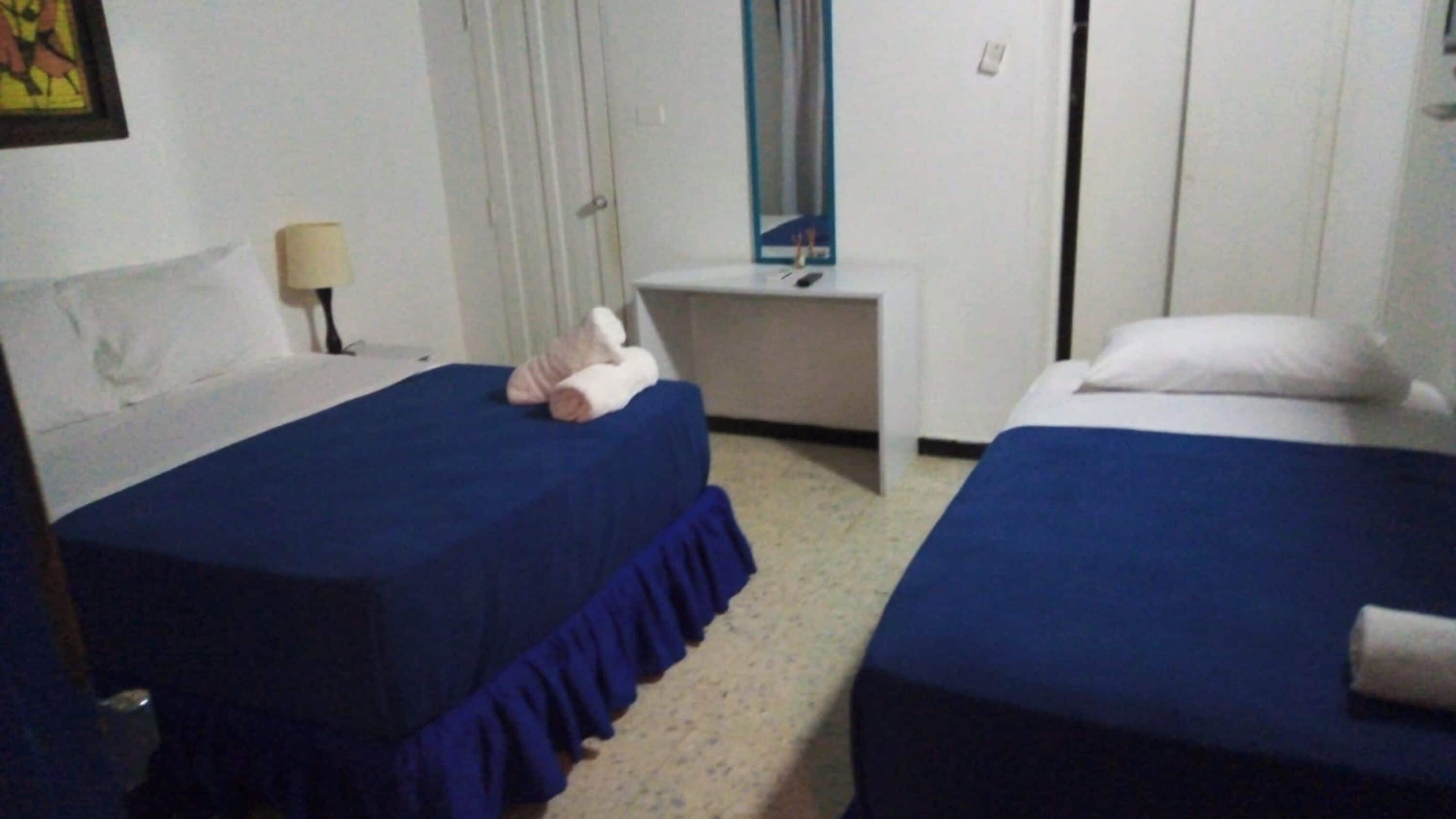 Una habitación de hotel con dos camas individuales, una mesita de noche, una lámpara y un espejo.