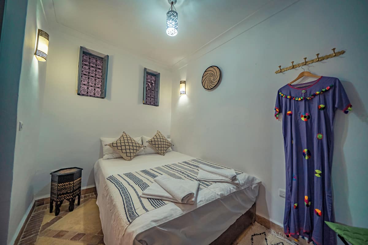 A bedroom with a bed, pillows, a hanging garment, and wall-mounted lights.
