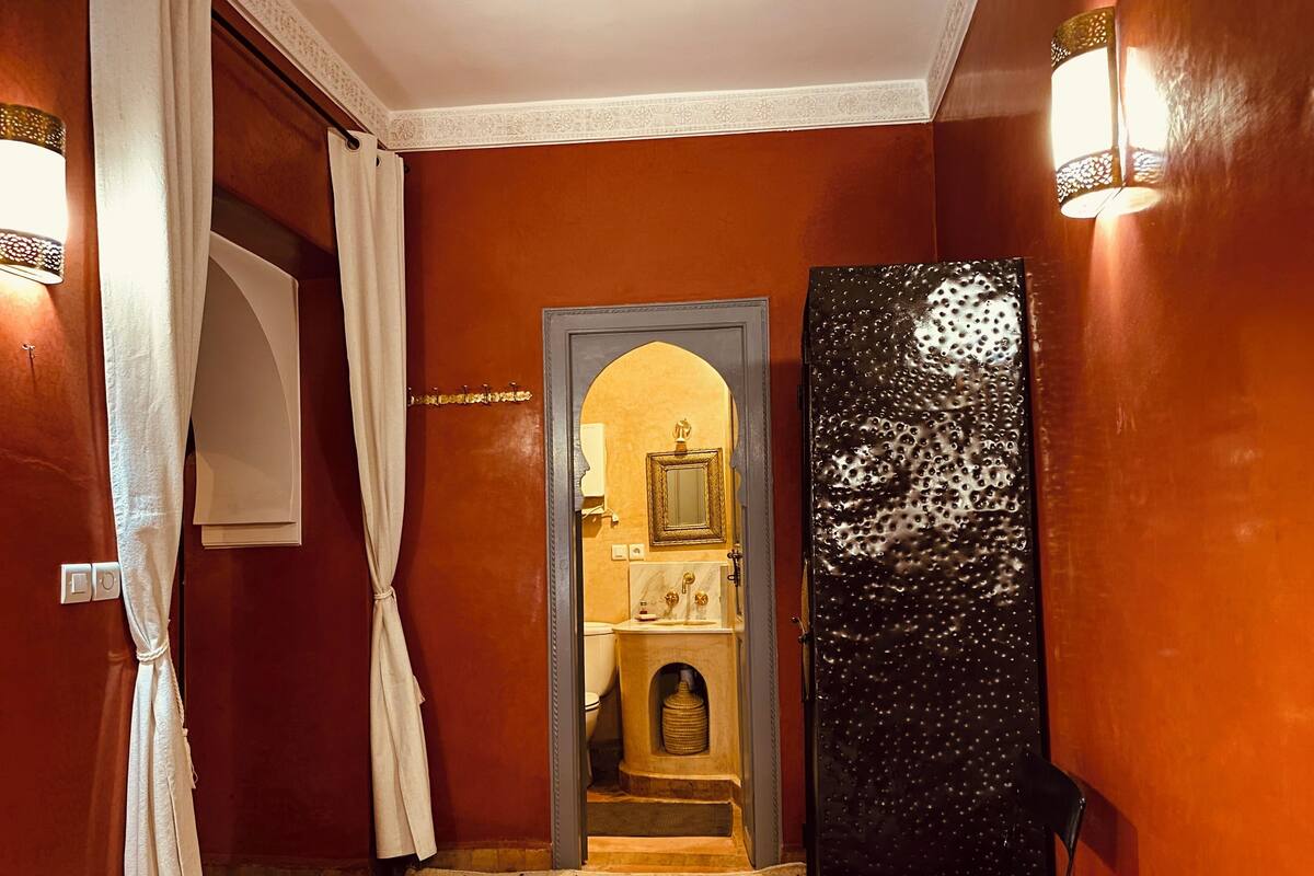 A hotel room with a checkered floor, a bed, a nightstand, a mirror, and a door leading to a bathroom.