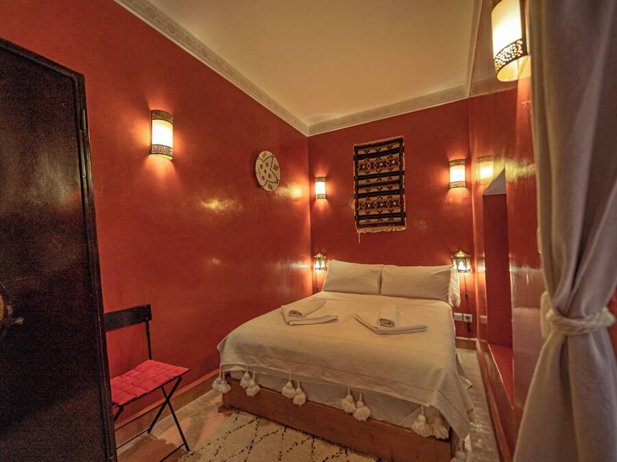 A bedroom with a bed, a chair, a wall clock, and decorative wall lights.