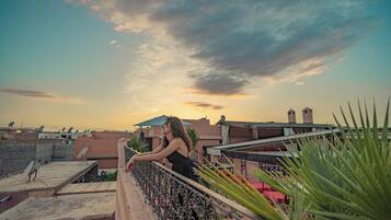 A rooftop terrace with a railing, satellite dishes, and a sunset view.