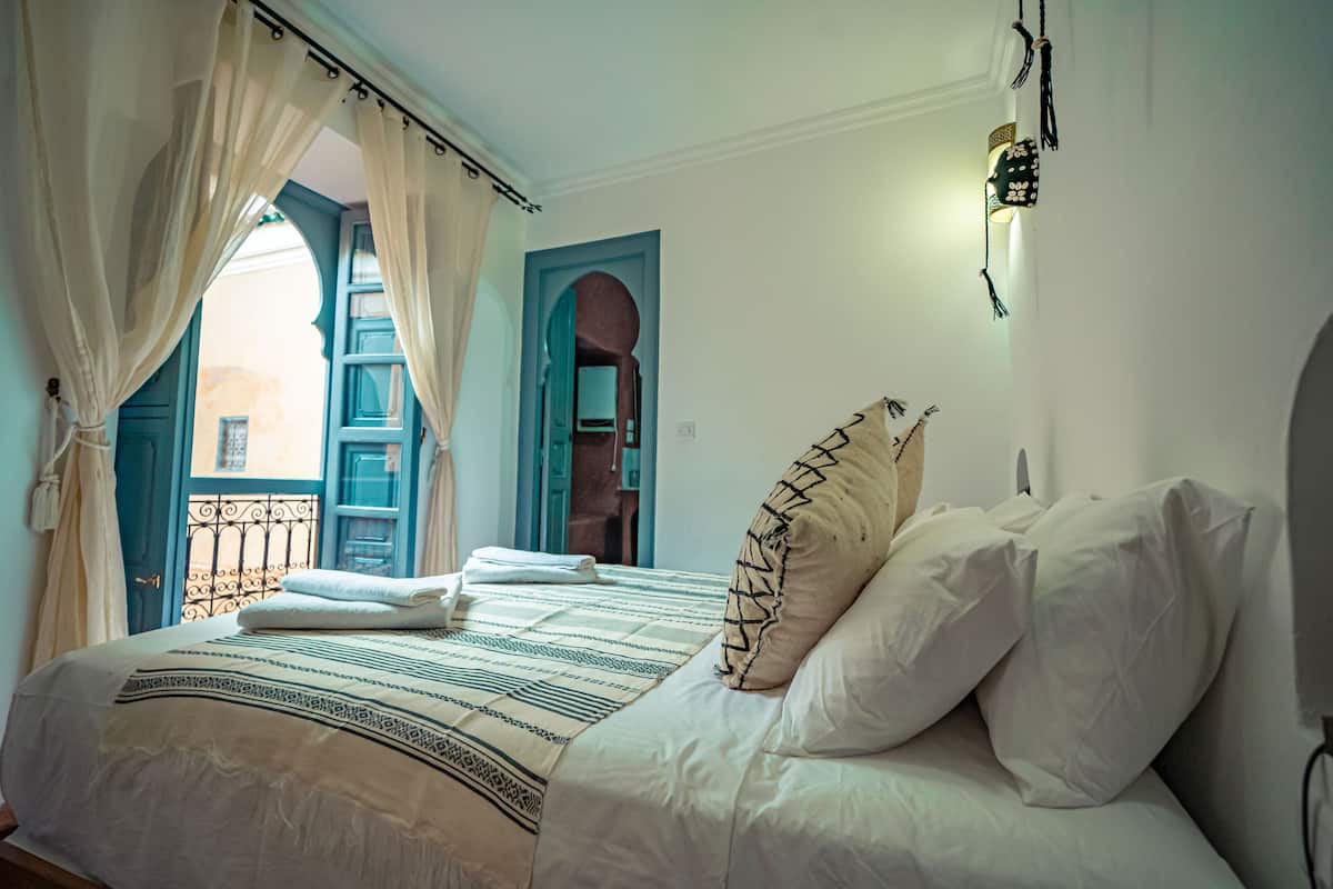 A bedroom with a bed, white pillows, a patterned bedspread, and a view through an open door.