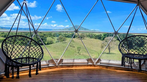 A geodesic dome structure with a view of a green landscape and mountains.