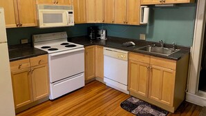 A kitchen with wooden cabinets, a white stove, a microwave, and a dishwasher. - Furnished efficiency for healthcare workers and executives in historic downtown. (Hannibal)