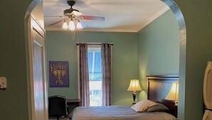 A bedroom with a bed, nightstand, lamp, ceiling fan, and a window with curtains. - Furnished efficiency for healthcare workers and executives in historic downtown. (Hannibal)