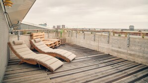 A rooftop terrace with wooden lounge chairs and a table, overlooking a cityscape. - Villa Viva Hotel Hamburg (Hamburg)