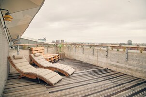 Eine Dachterrasse mit Holzliegen und einem Tisch, mit Blick auf eine Stadtlandschaft.