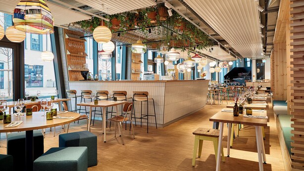 A restaurant interior with wooden tables, chairs, hanging plants, and pendant lights. - Villa Viva Hotel Hamburg (Hamburg)