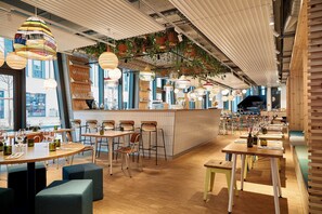 A restaurant interior with wooden tables, chairs, hanging plants, and pendant lights. - Villa Viva Hotel Hamburg (Hamburg)