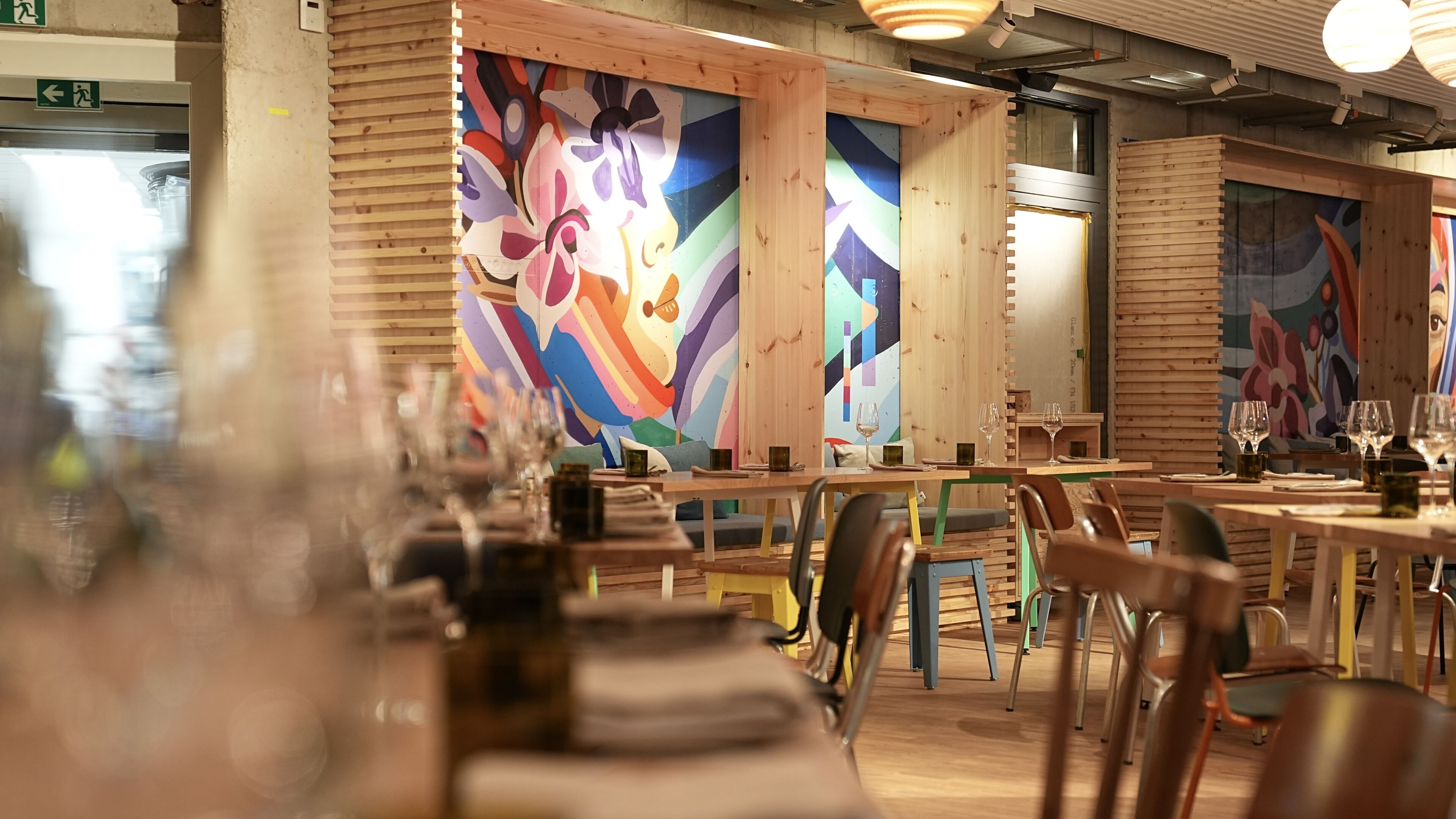 L’intérieur d’un restaurant avec des murs en bois, des peintures murales colorées et des tables dressées pour le service.