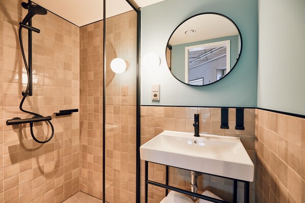 A modern bathroom with a glass-enclosed shower, a white sink, and a round mirror. - Villa Viva Hotel Hamburg (Hamburg)