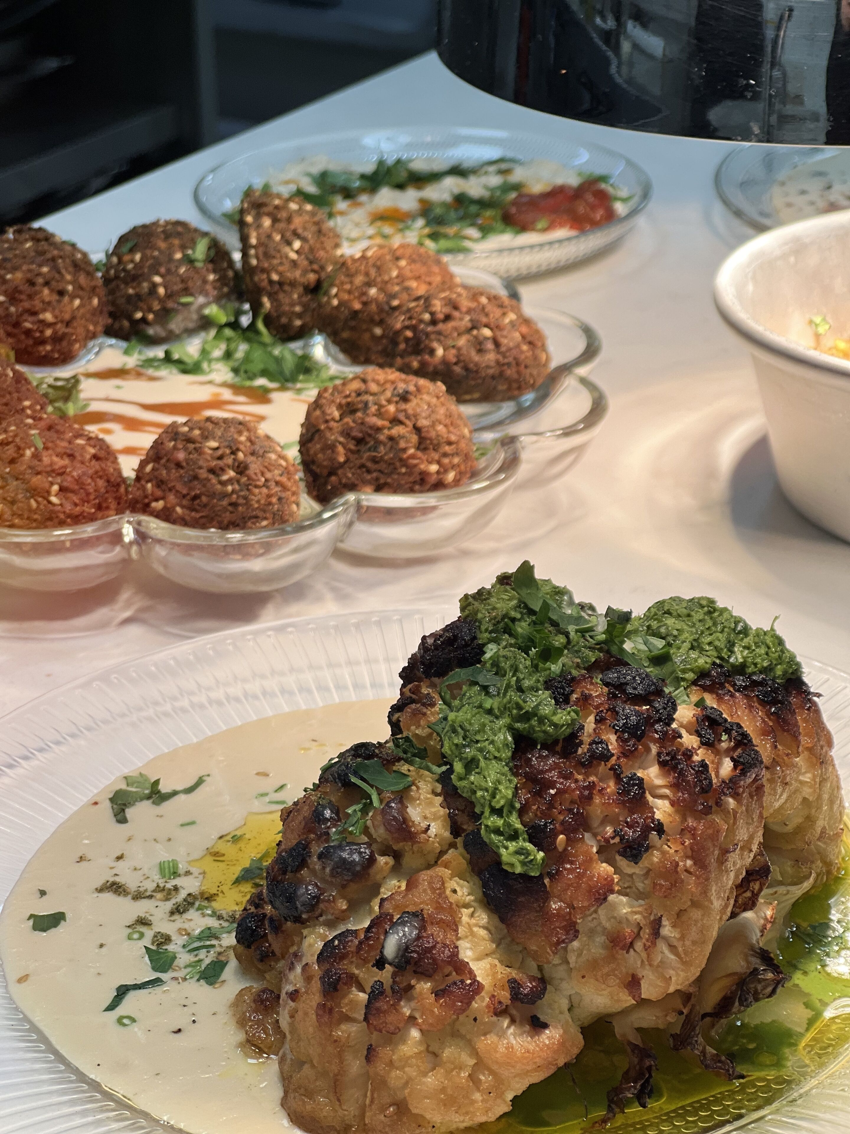 A table with various dishes including falafel, a grilled chicken breast, and a green sauce.