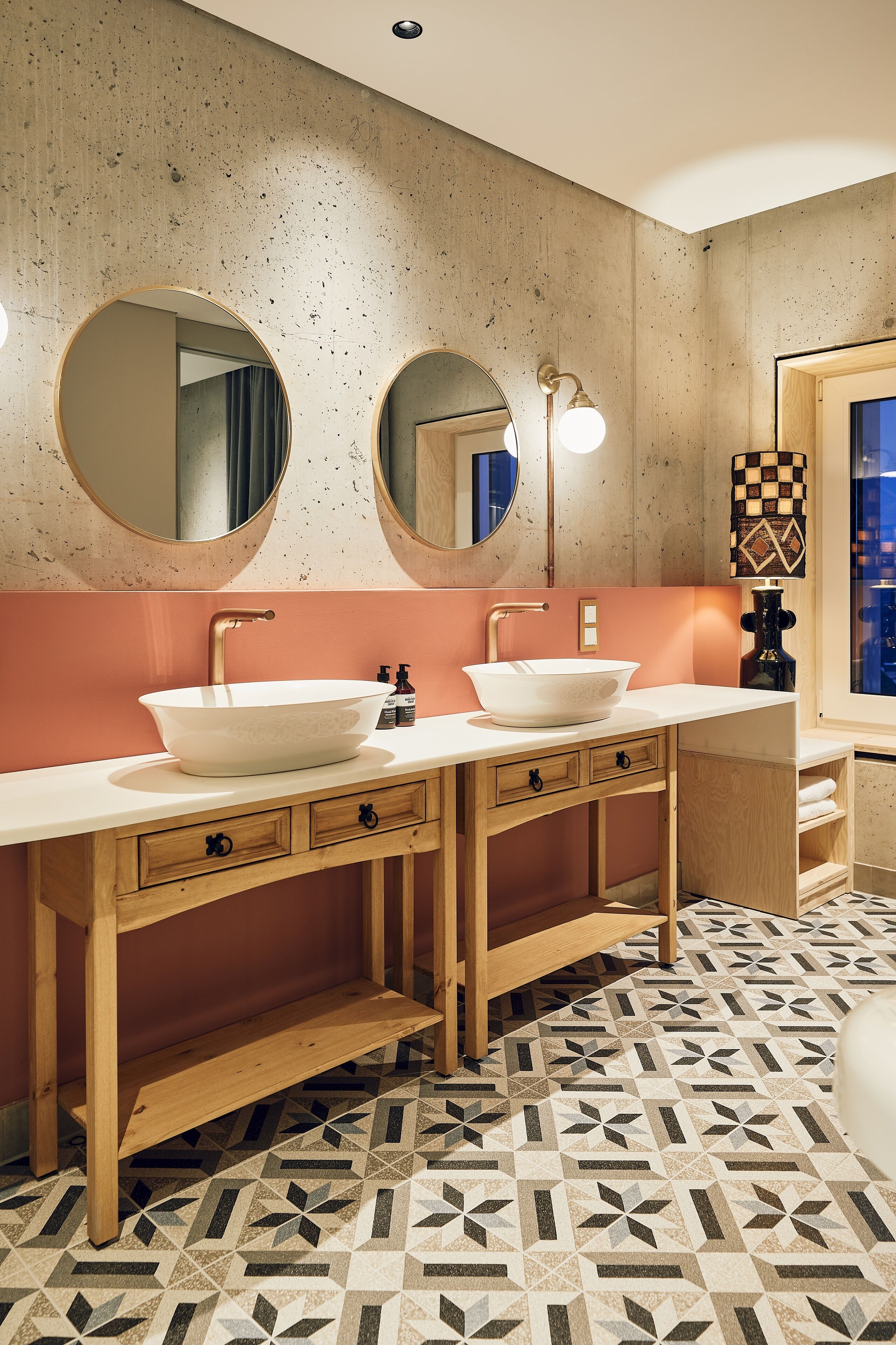 A bathroom with two sinks, wooden vanity, and patterned floor tiles.