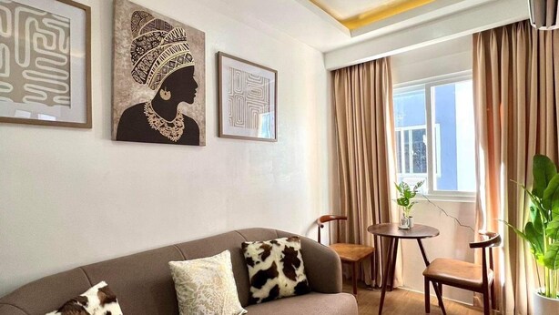 A living room with a sofa, a coffee table, and a chair. There are framed artworks on the wall and a window with curtains. - Escape to Paradise: Unwind in Style at our Spectacular Haven (Lapu-Lapu City)