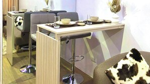 A modern living room with a dining area, a sofa with a cow-patterned pillow, and a table set for two. - Escape to Paradise: Unwind in Style at our Spectacular Haven (Lapu-Lapu City)