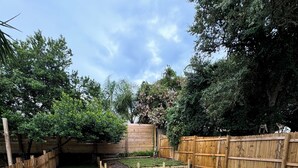Un patio trasero con terraza de madera, césped y valla de madera.