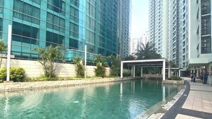A swimming pool with a tiled edge, surrounded by a low wall and palm trees. - Impressive City View Suit for 4 Persons (West Jakarta City)