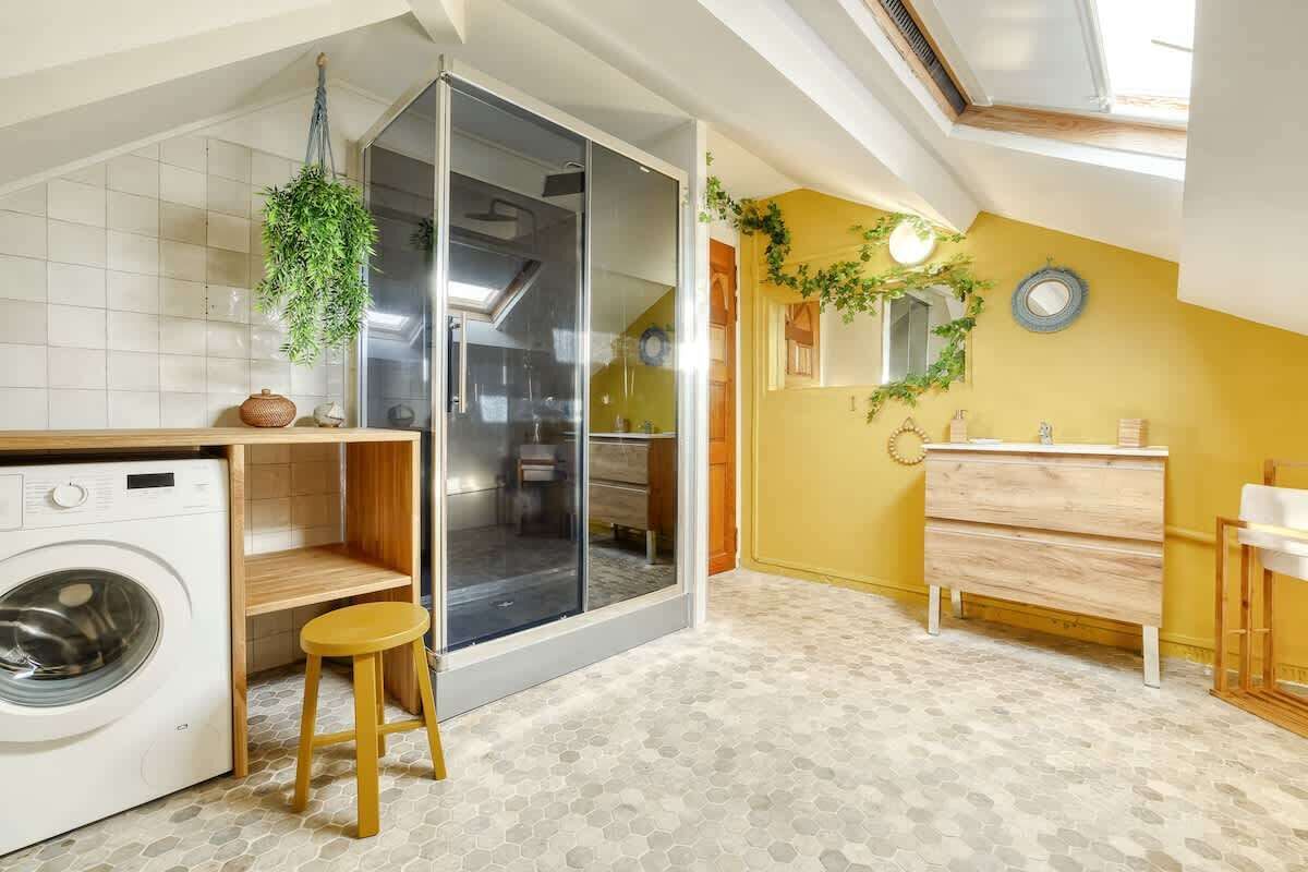 Une petite buanderie comprenant un lave-linge, un tabouret et une porte vitrée donnant sur la cuisine.
