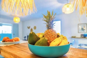 A bowl of fruit on a wooden table in a room with a blue wall and hanging light fixtures.